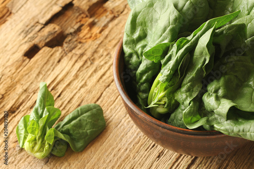 Fresh green leaves of spinach in a bowl on old wooden background.