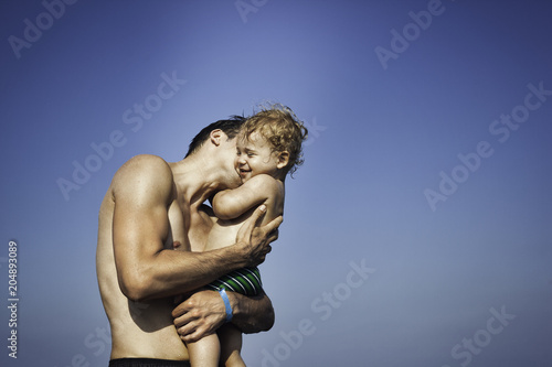 Father kissing his son on the beach against blue sky