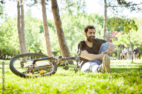 Bearded man looking away from the camera with his bicycle next to him in the park. Sport and health