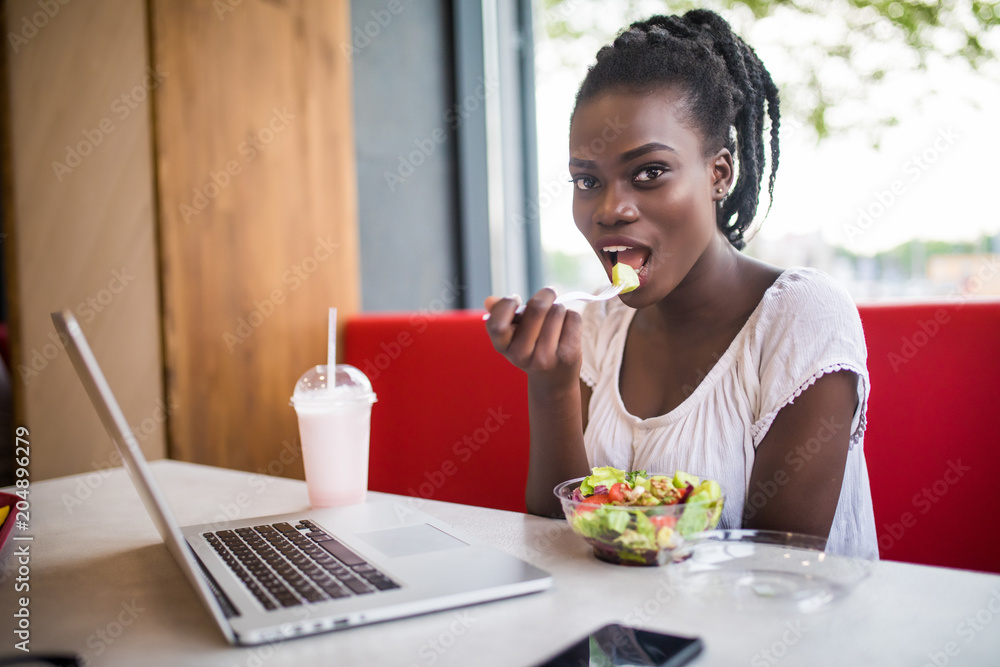 Beautiful woman have lanch eat salad at dinner sitting at cafe. Young african american woman sitting in a coffee shop and working on laptop. Beautiful woman have lanch eat salad at dinner sitting at cafe. Young african american woman sitting in a coffee shop and working on laptop.