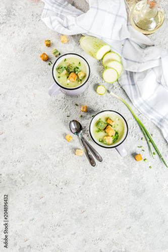 Two portions of homemade zucchini creamy soup with bread crumbs in mugs on a light concrete background. top view