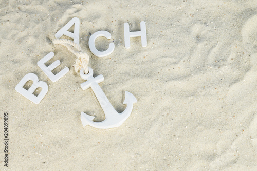 Fototapeta Naklejka Na Ścianę i Meble -  A white anchor in the sand, above it the word beach