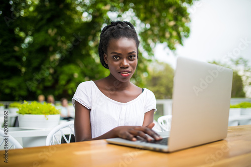 Young afro american black female freelancer working with digital tablet outdoors in cafe on a sunny day.