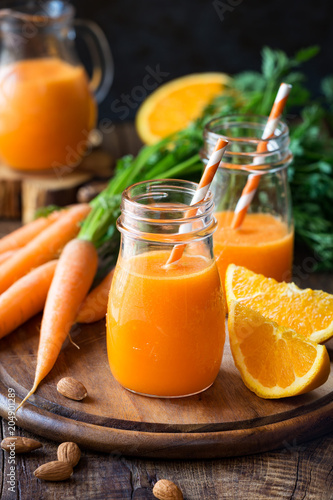 Healthy detox orange carrot smoothie or juice in glass jars on wooden background with fresh ingredients