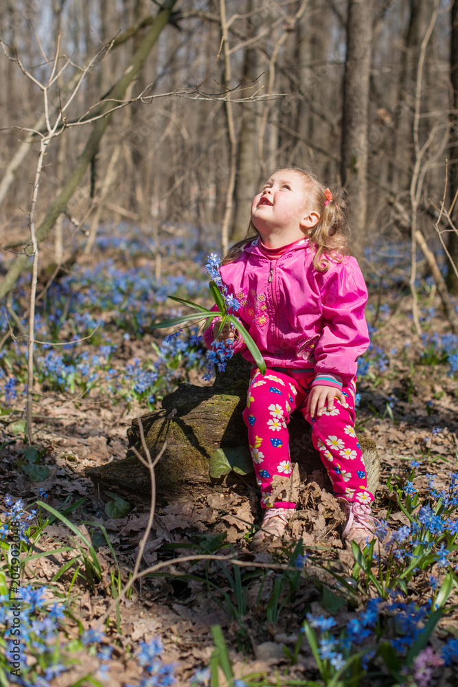 Little girl is smelling flowers while sitting on green meadow Little girl is smelling flowers while sitting on green meadow