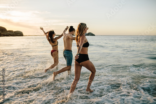 Friends holding hands and running at beach