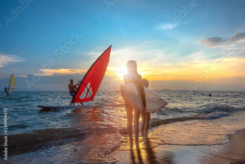 slim woman with family group father, sister are enjoy around with water sports such surfboard, windsurf, kitesurf in the sea beach at sunset scenery