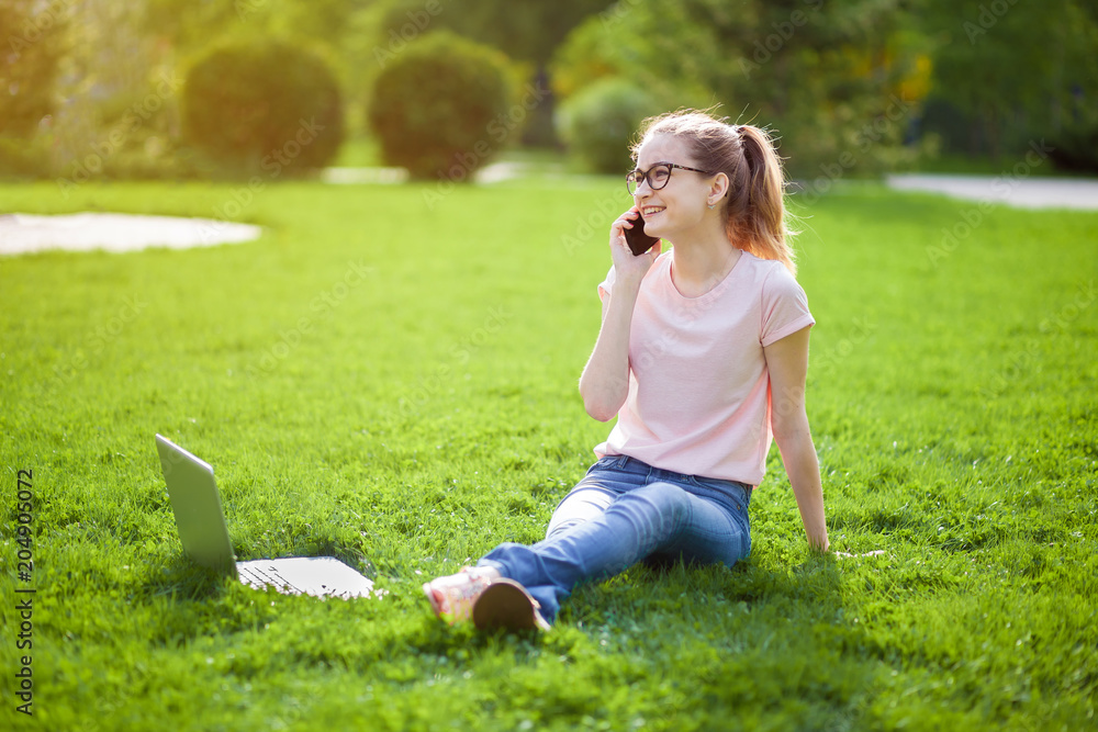 Girl with glasses talking on the phone sitting on the grass Girl with glasses talking on the phone sitting on the grass