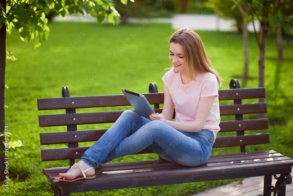 Obraz premium Girl with tablet sitting on a bench in the Park