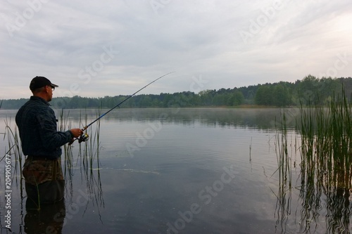 Fisherman standing in the lake and catching the fish at cloudy day.
