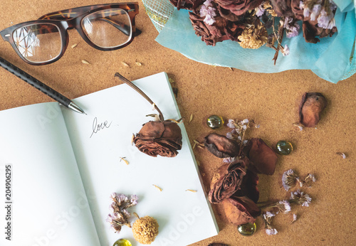 top view flat layer witerd old rusty brown roses and love word  on blank white book with blurry glasses and blue bouquet flower in background on crok wooden table, love forever, memory concept photo