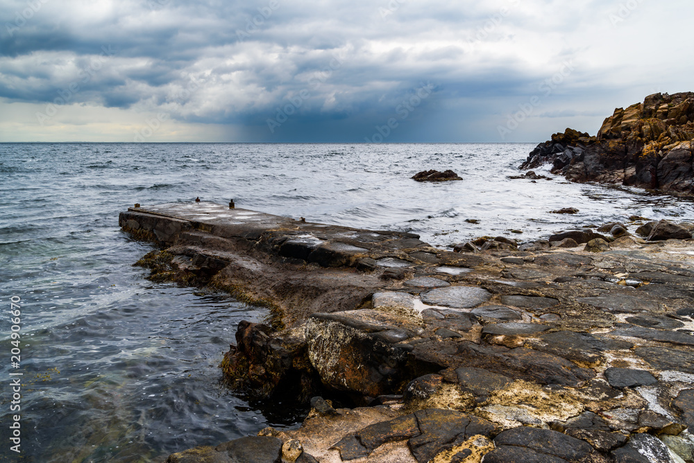 Western Kullaberg nature reserve, Sweden - Storm clouds approaching over the small stone pier in the rocky landscape.