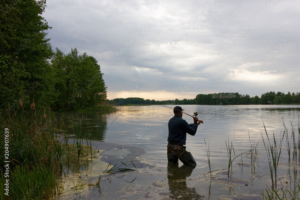 Fisherman standing in the lake and catching the fish at cloudy day. Fisherman standing in the lake and catching the fish at cloudy day.