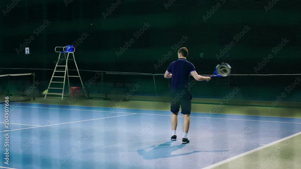 Serve by professional tennis player. Tennis serve indoor of tenis hall. Man on serve with tenis racket and dressed in black t-shirt, black shorts and black shoes. Serve by professional tennis player. Tennis serve indoor of tenis hall. Man on serve with tenis racket and dressed in black t-shirt, black shorts and black shoes.
