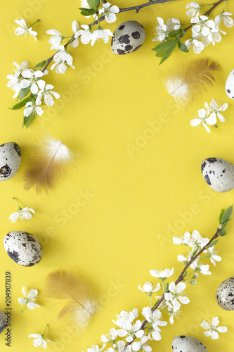 Easter background with eggs and blossom over light yellow pastel background, top view with space for your text.