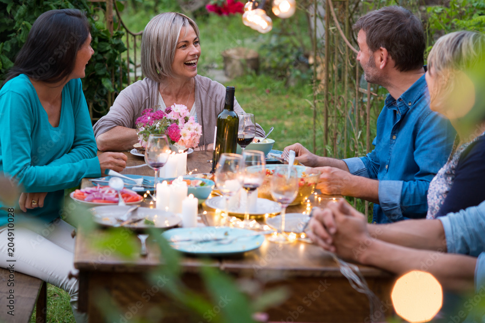 Group of friends gathered around a table in a garden on a summer evening to share a meal and have a good time together Group of friends gathered around a table in a garden on a summer evening to share a meal and have a good time together