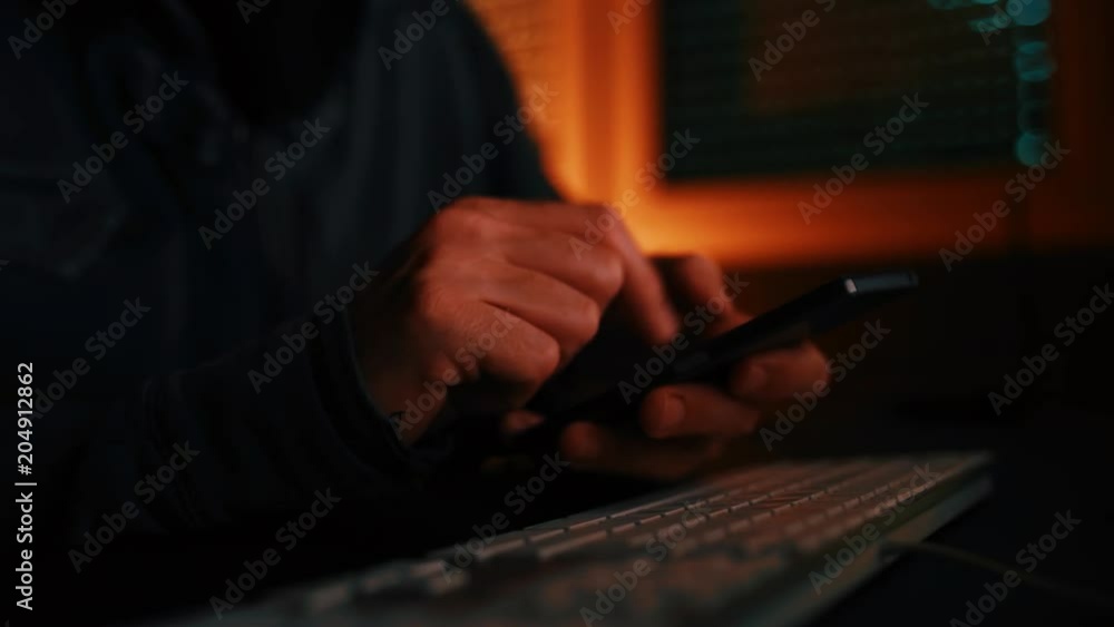 Computer hacker using smartphone device in dark interior, low key footage Computer hacker using smartphone device in dark interior, low key footage
