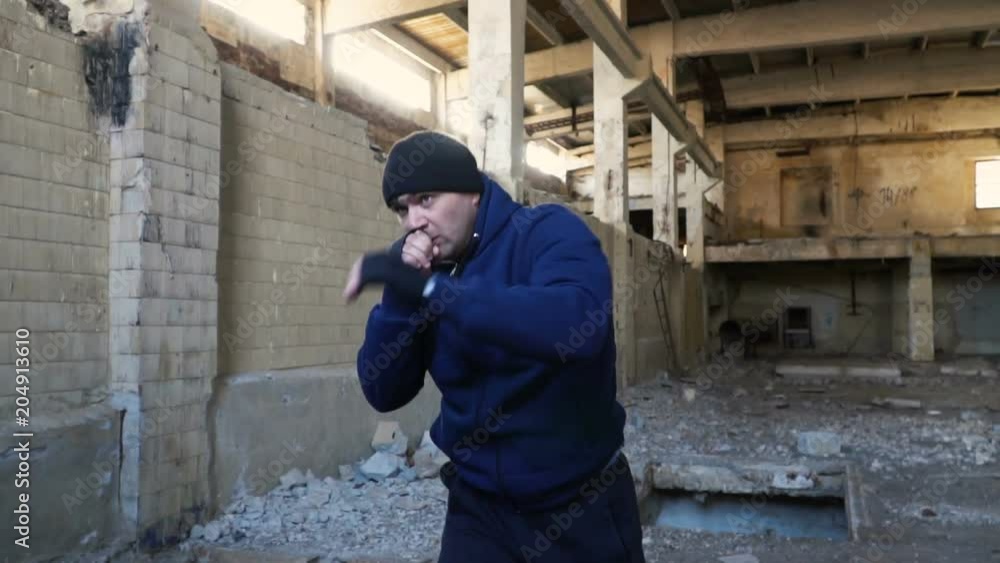 A fight with a shadow. A boxer in a blue sweatshirt trains in an abandoned building. Slow motion. A fight with a shadow. A boxer in a blue sweatshirt trains in an abandoned building. Slow motion.