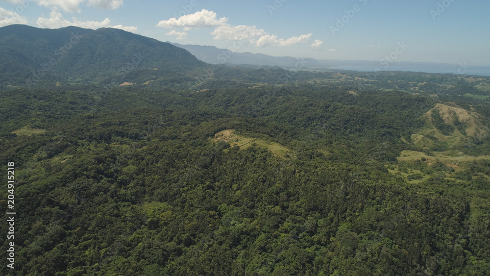 Aerial view of mountains covered with green forest, trees with blue sky. Philippines, Pagudpud, Luzon. Tropical landscape in Asia.
