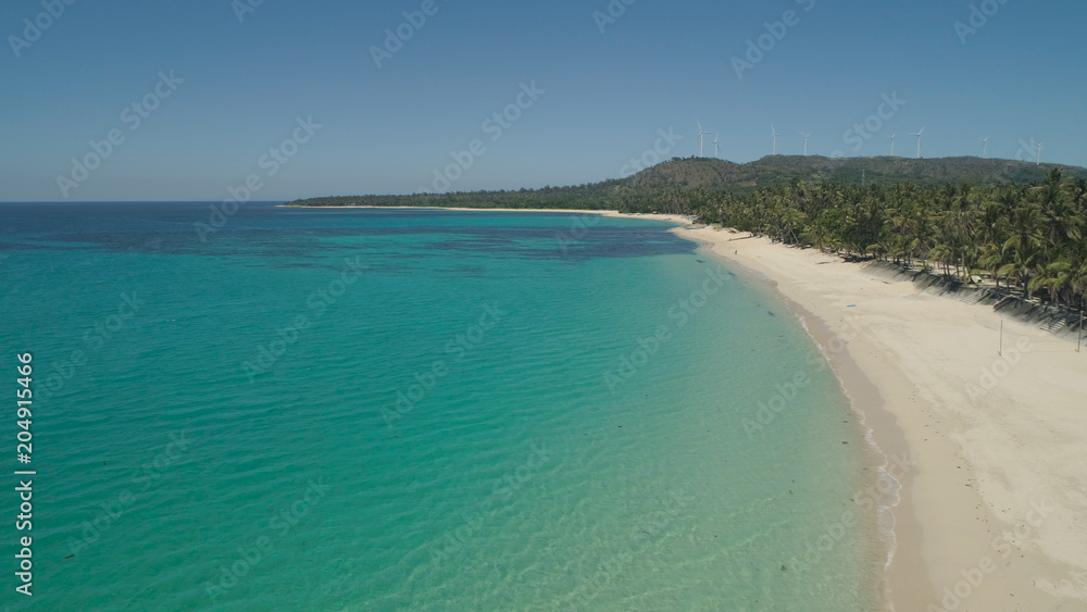 Fototapeta premium Aerial view of beautiful tropical beach Saud with turquoise water in blue lagoon, Pagudpud, Philippines. Ocean coastline with sandy beach and palm trees. Tropical landscape in Asia.