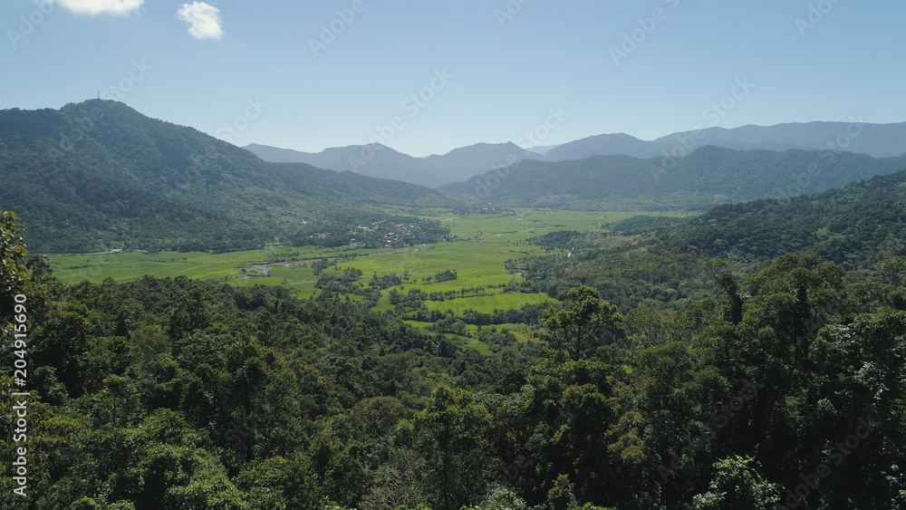 Mountain valley with village, farmland, rice fields. Aerial view of Mountains with green tropical rainforest, trees, jungle with blue sky. Philippines, Luzon.
