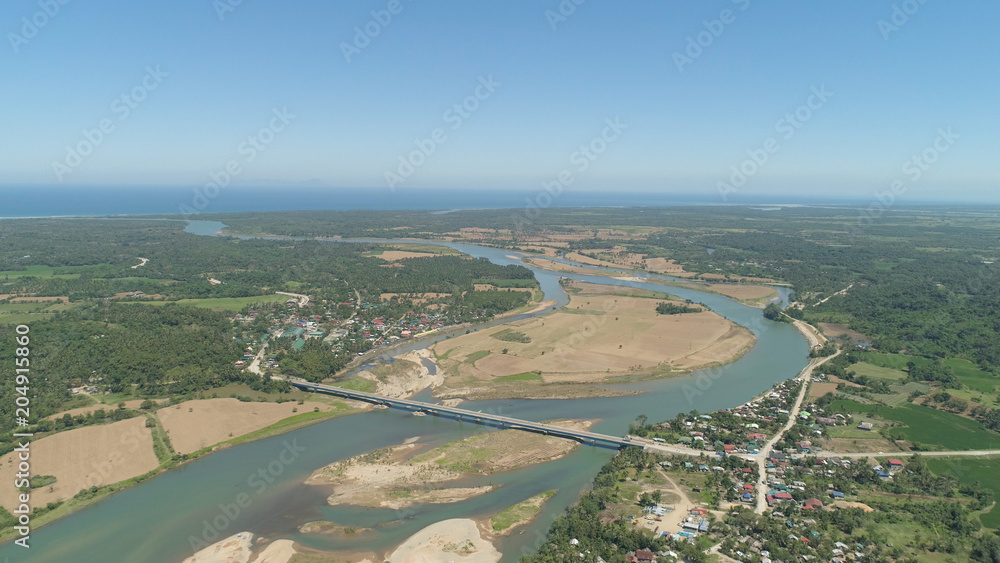 River passing through farmlands and flowing into sea. Philippines, Luzon. Aerial view of river, agricultural land against blue sky.