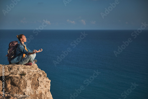 Profile of calm woman with closed eyes sitting in lotus pose on high. Deep ocean on background. Copy space in right side