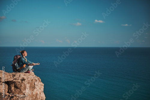Profile of enjoyed camper relaxing on stony mountain in yoga pose. Blue ocean on background. Copy space in right side