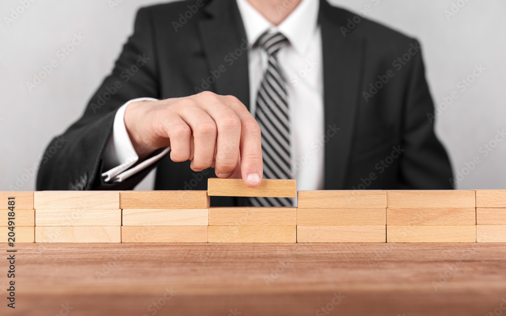 Close-up of businessman completing building wall of wooden bricks on table, copy space. Close-up of businessman completing building wall of wooden bricks on table, copy space.