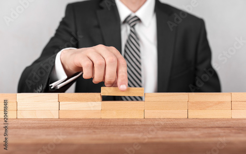 Close-up of businessman completing building wall of wooden bricks on table, copy space.