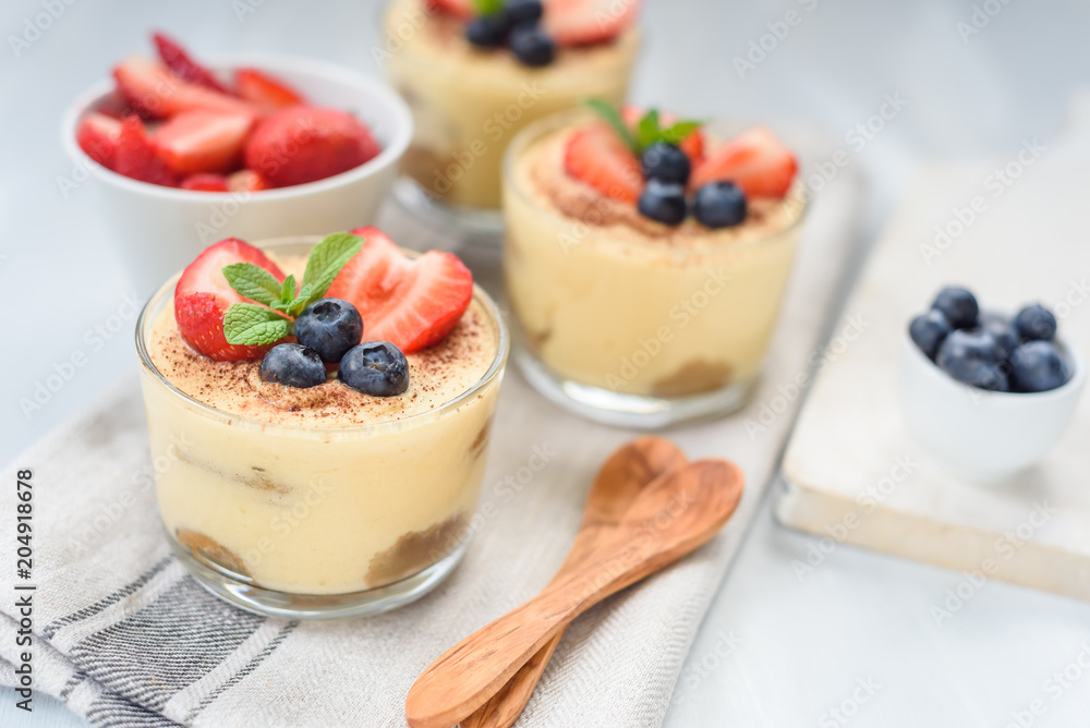 homemade, exquisite dessert tiramisu in glasses decorated with strawberry, blueberry, mint on white wooden table homemade, exquisite dessert tiramisu in glasses decorated with strawberry, blueberry, mint on white wooden table