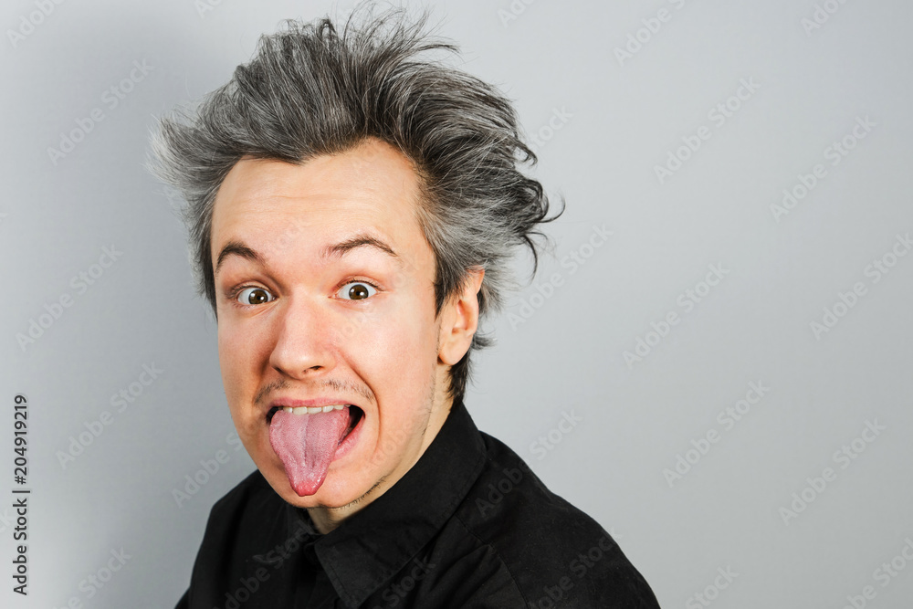 Young guy shows tongue like Albert Einstein on gray background. Young guy shows tongue like Albert Einstein on gray background.