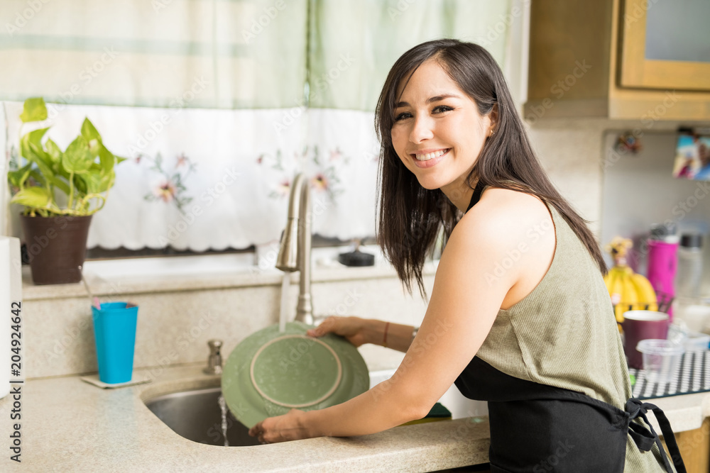 Portrait of a happy woman cleaning utensils in kitchen sink Portrait of a happy woman cleaning utensils in kitchen sink