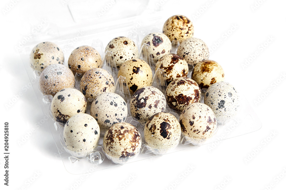 Quail spotted eggs in a transparent plastic container on white background