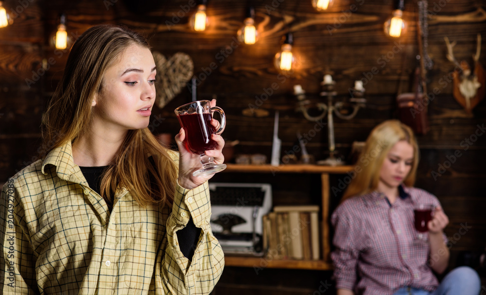 Friends on relaxed faces in plaid clothes relaxing, defocused. Friends enjoy mulled wine in warm atmosphere, wooden interior. Girls relaxing and drinking mulled wine. Rest and relax concept Friends on relaxed faces in plaid clothes relaxing, defocused. Friends enjoy mulled wine in warm atmosphere, wooden interior. Girls relaxing and drinking mulled wine. Rest and relax concept
