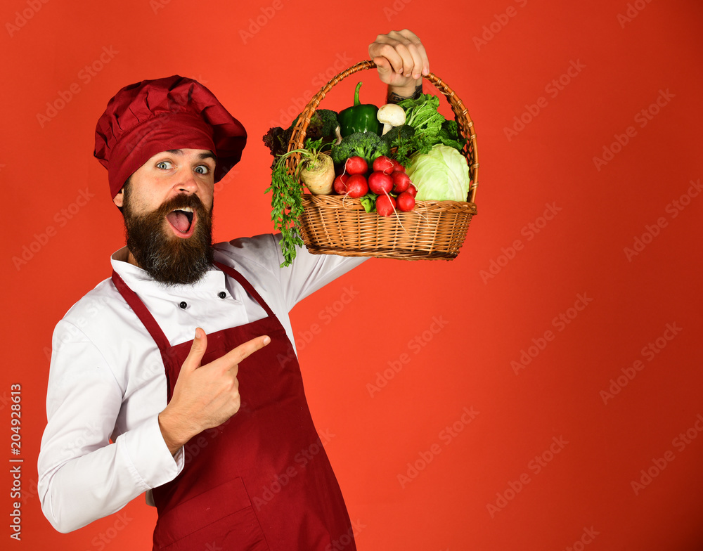 Cook with happy face in burgundy uniform points at vegetables Cook with happy face in burgundy uniform points at vegetables