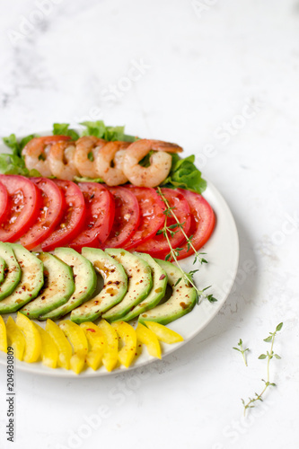 Avocado salad on a white background. Avocado, tomato, pepper and shrimps on a plate lined with rows © allenkayaa