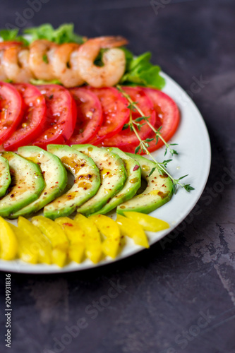 Avocado, tomato, pepper and shrimps on a plate lined with rows. Avocado salad on a dark background © allenkayaa