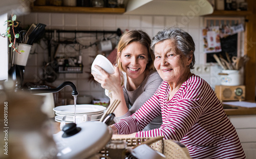 Fotografie An elderly grandmother with an adult granddaughter at home, washing the dishes
