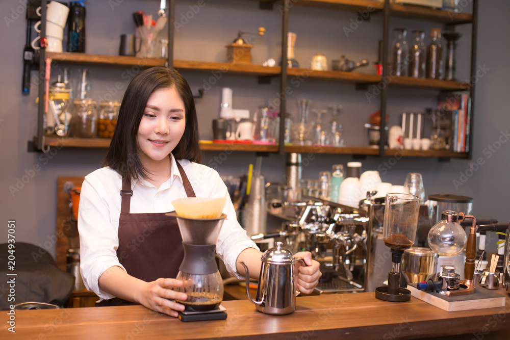 Asian women Barista smiling and looking to camera in coffee shop counter.  Barista female working at cafe. Working woman small business owner or sme concept.