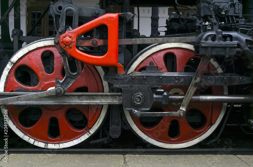 fragment of vintage functioning steam locomotive standing at station, closeup, visible driving wheels with a system of pistons, connecting rods and levers..