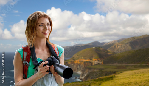 travel, tourism and photography concept - happy young woman with backpack and camera photographing over bixby creek bridge on big sur coast of california background © Syda Productions