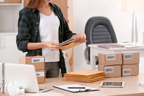 Young woman preparing parcel envelopes for shipment to client in home office