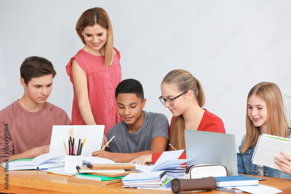 Group of teenagers doing homework with teacher in classroom Group of teenagers doing homework with teacher in classroom