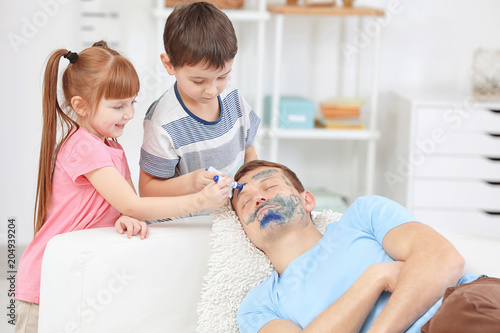 Little children painting their father's face while he sleeping. April fool's day prank photo