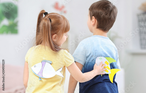 Cuadro en lienzo Little girl sticking paper fish to boy's back indoors