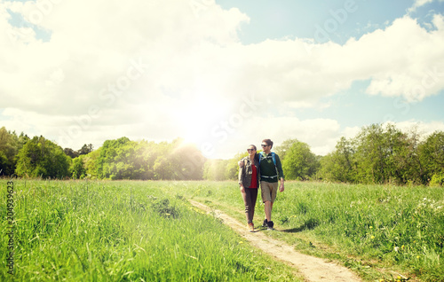 travel, hiking, backpacking, tourism and people concept - happy couple with backpacks hugging and walking along country road