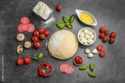 Flat lay composition with raw dough and ingredients for pizza on grey background