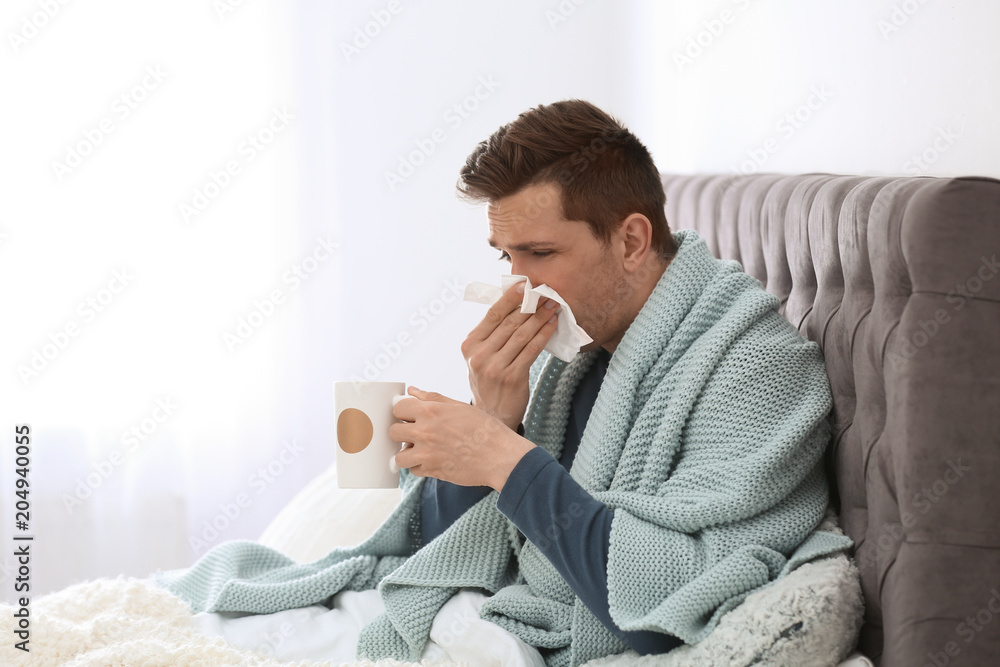 Sick young man with cup of hot drink and tissue suffering from cold in bed Sick young man with cup of hot drink and tissue suffering from cold in bed