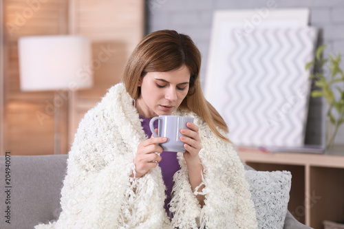 Sick woman with cup of hot drink suffering from cold on sofa at home